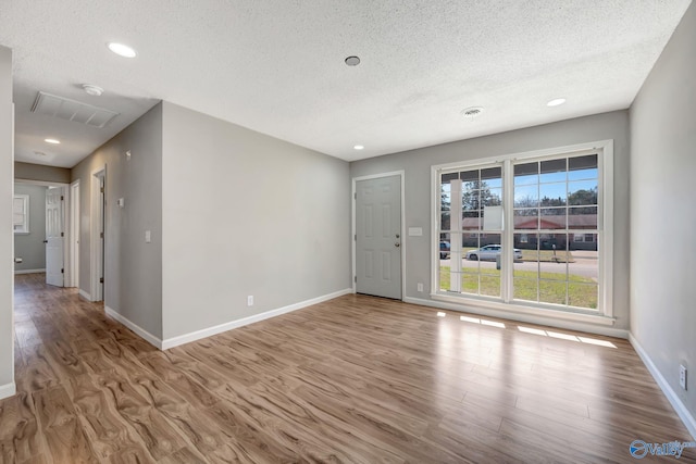 spare room featuring a textured ceiling, baseboards, wood finished floors, and recessed lighting