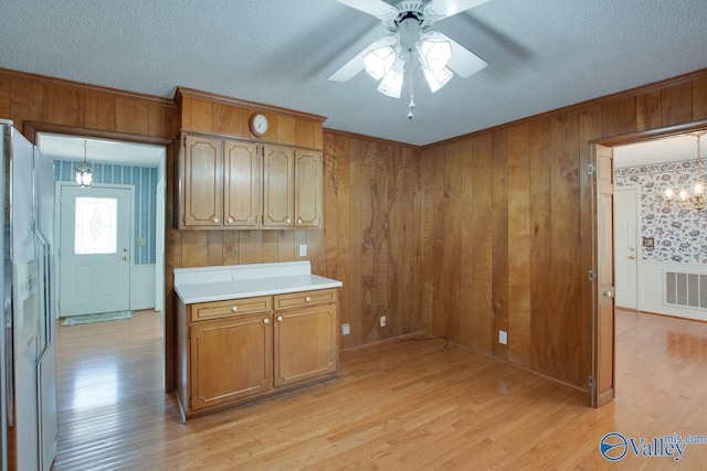 kitchen featuring ceiling fan with notable chandelier, wood walls, light wood-type flooring, and white refrigerator with ice dispenser