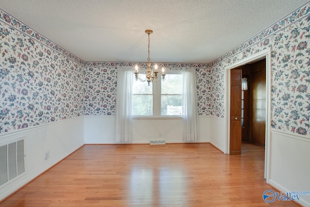 unfurnished dining area featuring a chandelier, light hardwood / wood-style floors, and a textured ceiling