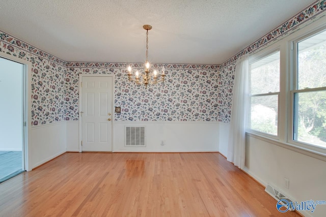 unfurnished dining area featuring a notable chandelier, light hardwood / wood-style floors, and a textured ceiling