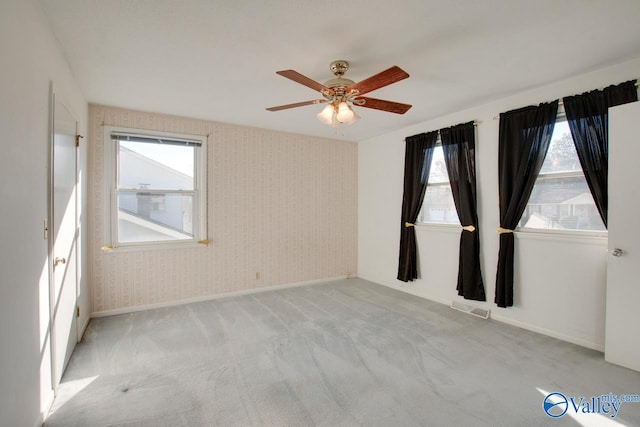 spare room featuring light colored carpet, a wealth of natural light, and ceiling fan