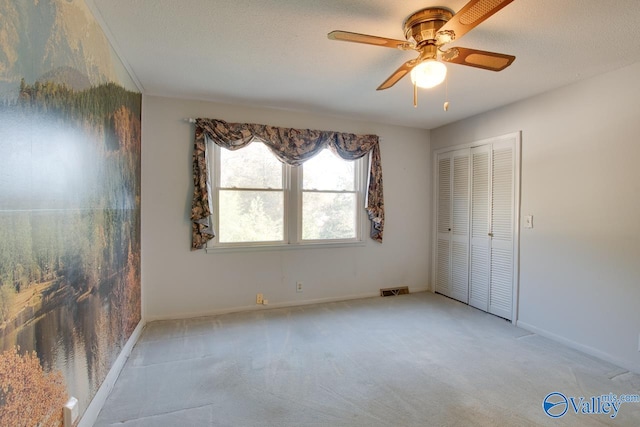 unfurnished bedroom with ceiling fan, a closet, light colored carpet, and a textured ceiling