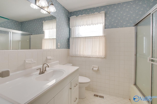 full bathroom with tile patterned flooring, toilet, shower / bath combination with glass door, vanity, and tile walls