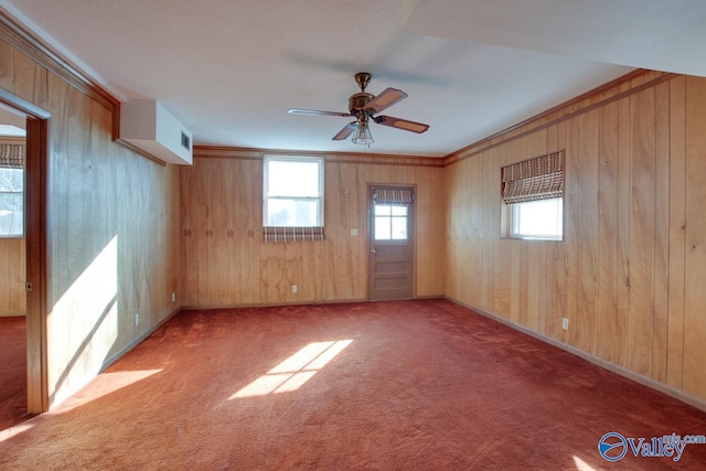 carpeted empty room with ceiling fan, crown molding, and wood walls