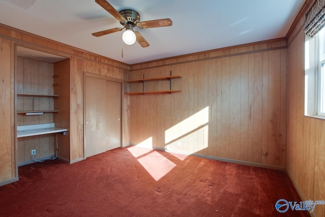 unfurnished bedroom with dark carpet, built in desk, wooden walls, and a closet