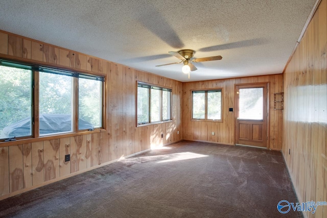 carpeted empty room featuring ceiling fan, a textured ceiling, and wooden walls