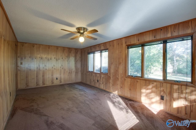 carpeted spare room featuring wooden walls, ceiling fan, and a textured ceiling