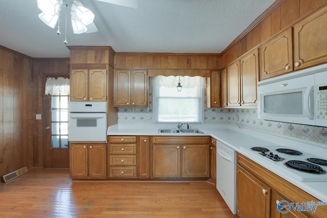 kitchen with white appliances, sink, wooden walls, and light hardwood / wood-style flooring