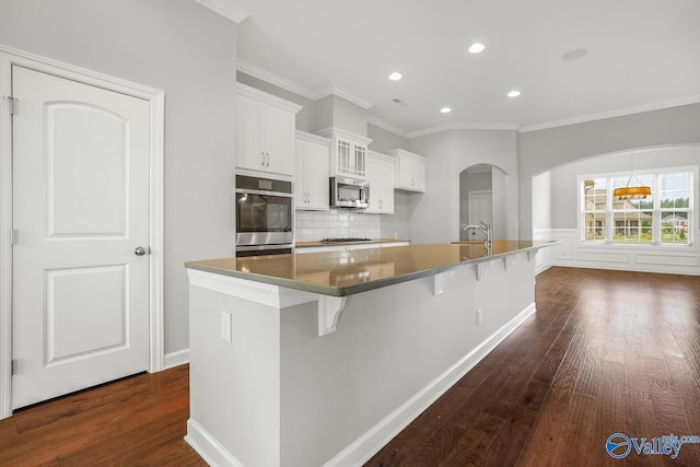 kitchen featuring dark wood-type flooring, a breakfast bar, white cabinetry, stainless steel appliances, and a spacious island