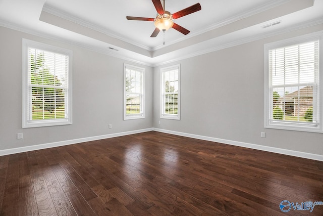 empty room featuring ornamental molding, plenty of natural light, dark hardwood / wood-style flooring, and a tray ceiling