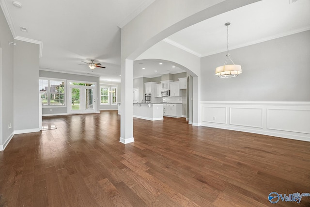 unfurnished living room with crown molding, dark wood-type flooring, and ceiling fan