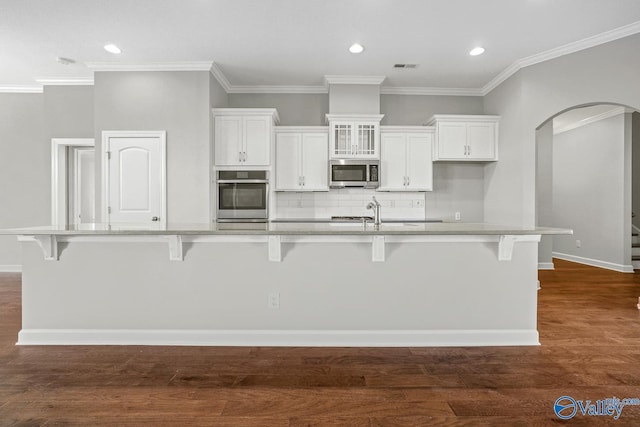 kitchen featuring white cabinetry, a breakfast bar area, a large island with sink, stainless steel appliances, and dark wood-type flooring