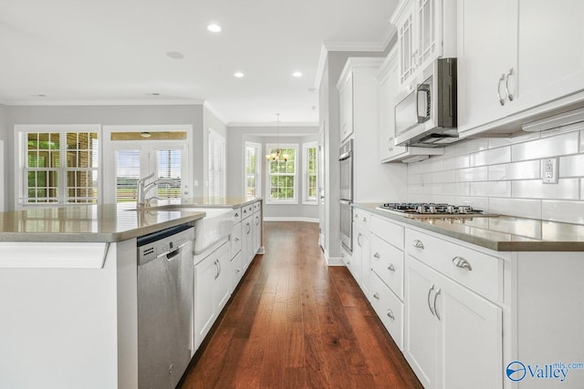 kitchen featuring white cabinetry, decorative backsplash, ornamental molding, stainless steel appliances, and a center island with sink