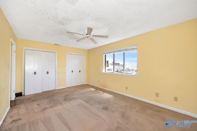 unfurnished bedroom featuring carpet flooring, a ceiling fan, two closets, a textured ceiling, and baseboards