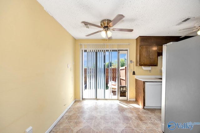 kitchen with freestanding refrigerator, a textured ceiling, dishwasher, ceiling fan, and baseboards