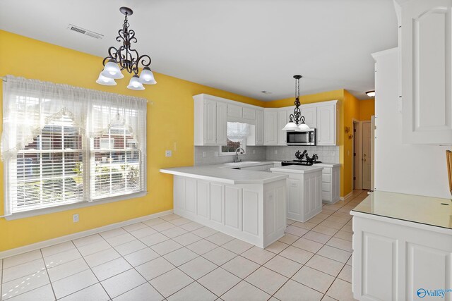 kitchen featuring sink, kitchen peninsula, backsplash, a chandelier, and white cabinetry