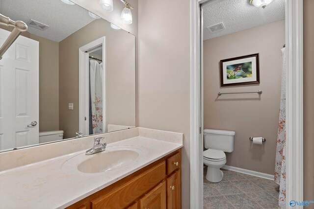 bathroom featuring vanity, toilet, a textured ceiling, and tile patterned floors