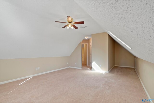 additional living space with lofted ceiling, light colored carpet, ceiling fan, and a textured ceiling