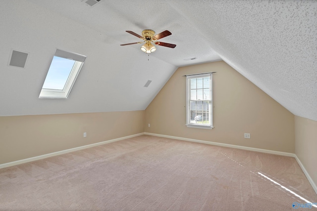 bonus room with vaulted ceiling with skylight, ceiling fan, light colored carpet, and a textured ceiling