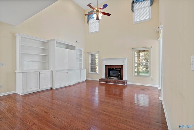 unfurnished living room with a brick fireplace, built in features, ceiling fan, high vaulted ceiling, and hardwood / wood-style flooring