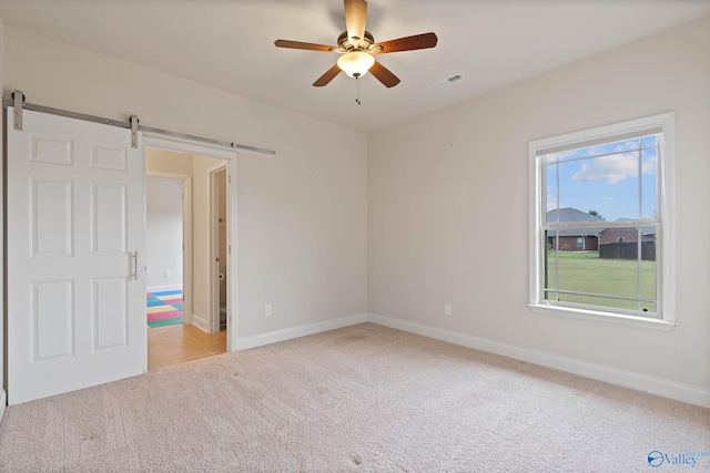 carpeted spare room with a barn door and ceiling fan