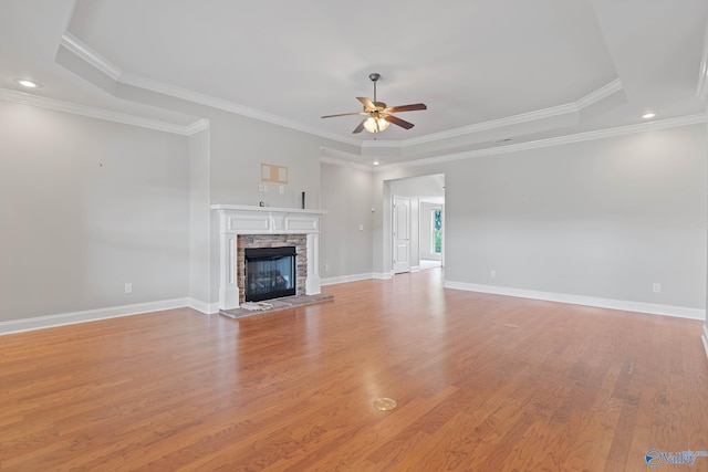 unfurnished living room with a fireplace, light wood-type flooring, a raised ceiling, ceiling fan, and ornamental molding