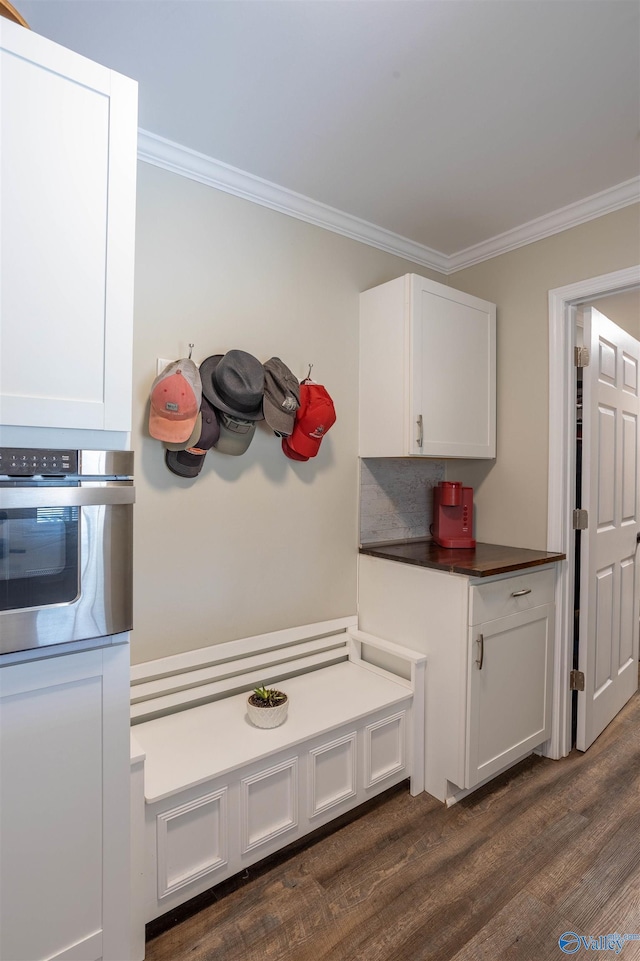 kitchen with dark wood-type flooring, white cabinetry, ornamental molding, oven, and decorative backsplash