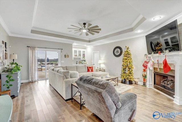 living room with light wood-type flooring, a tray ceiling, and crown molding