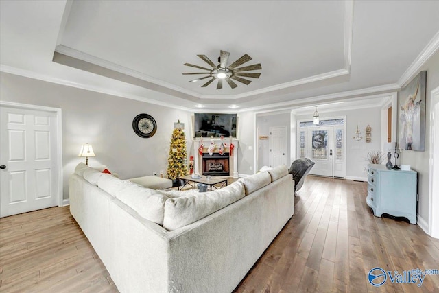 living room with hardwood / wood-style floors, ceiling fan, crown molding, and a tray ceiling