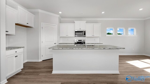 kitchen with light stone countertops, white cabinetry, a kitchen island with sink, and appliances with stainless steel finishes