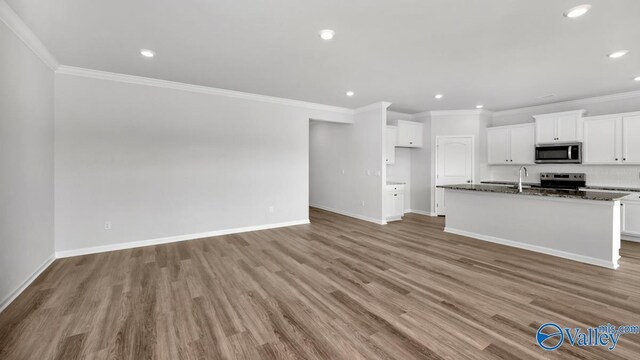 kitchen with dark stone counters, stainless steel appliances, a kitchen island with sink, light hardwood / wood-style flooring, and white cabinets