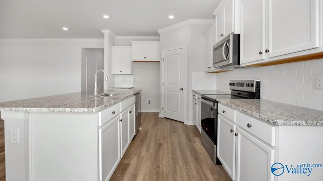 kitchen featuring white cabinetry, sink, stainless steel appliances, light hardwood / wood-style floors, and a center island with sink