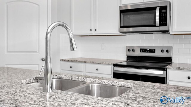 kitchen featuring white cabinets, sink, decorative backsplash, light stone countertops, and stainless steel appliances