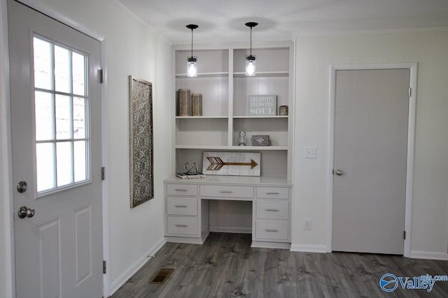 unfurnished office featuring dark wood-type flooring, ornamental molding, built in desk, and built in shelves