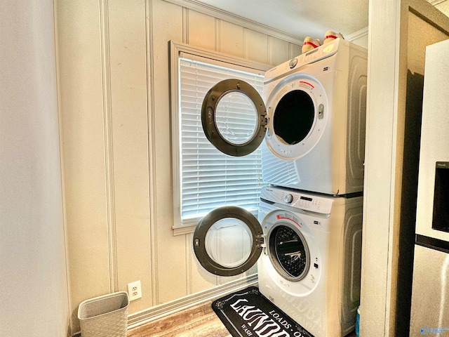 laundry room featuring crown molding, stacked washer and dryer, and wood-type flooring