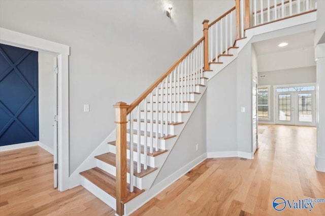 stairs with a towering ceiling, hardwood / wood-style floors, and french doors