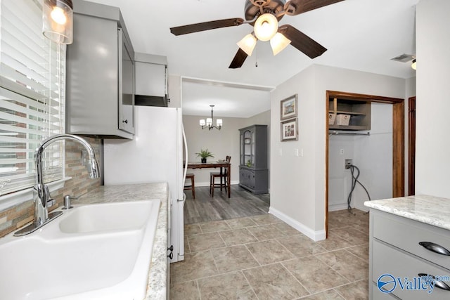 kitchen featuring sink, gray cabinetry, tasteful backsplash, light tile patterned flooring, and ceiling fan with notable chandelier