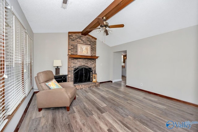 living room with hardwood / wood-style floors, lofted ceiling with beams, ceiling fan, a brick fireplace, and a textured ceiling