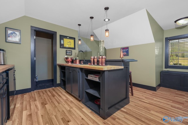 kitchen featuring vaulted ceiling, sink, light wood-type flooring, pendant lighting, and kitchen peninsula