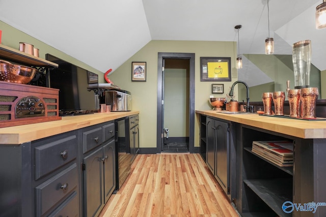 kitchen with light hardwood / wood-style flooring, hanging light fixtures, butcher block counters, vaulted ceiling, and sink