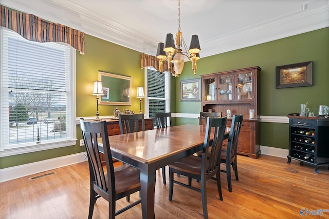 dining area featuring a chandelier, visible vents, baseboards, light wood finished floors, and crown molding