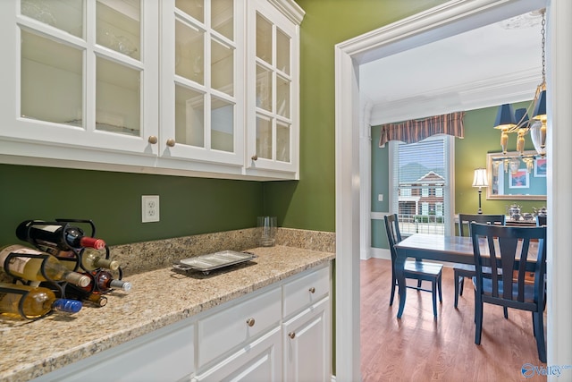 kitchen featuring light stone counters, white cabinetry, light wood-style floors, ornamental molding, and glass insert cabinets