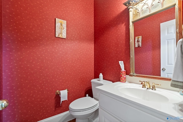 half bathroom featuring toilet, wallpapered walls, and vanity