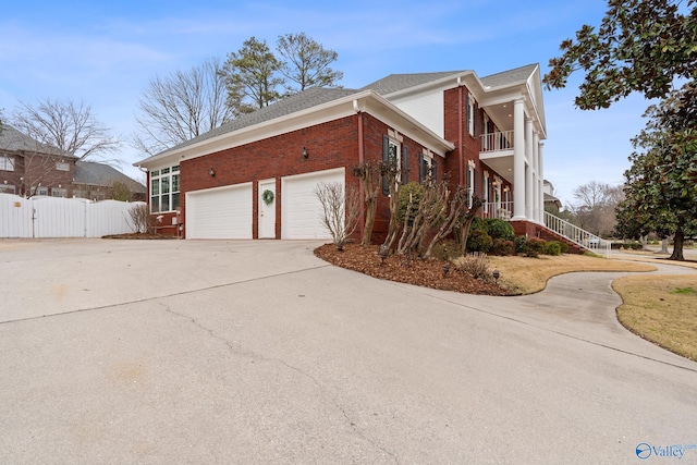 view of side of property featuring brick siding, concrete driveway, stairway, fence, and a balcony