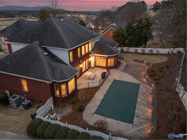 back of property at dusk featuring brick siding, a patio, cooling unit, a fenced backyard, and driveway