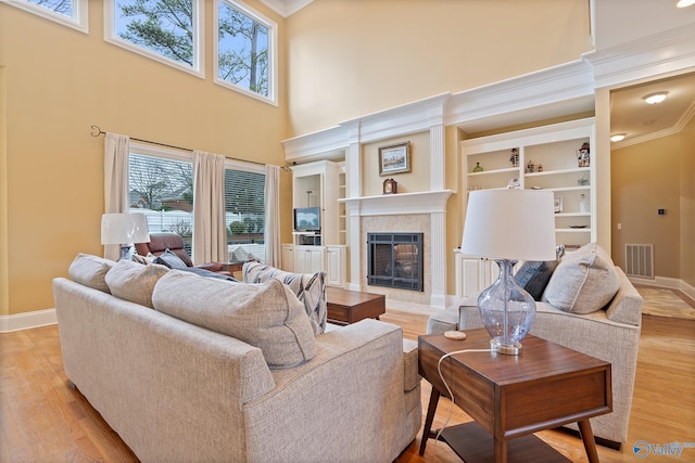 living room featuring a fireplace, visible vents, ornamental molding, light wood-type flooring, and baseboards