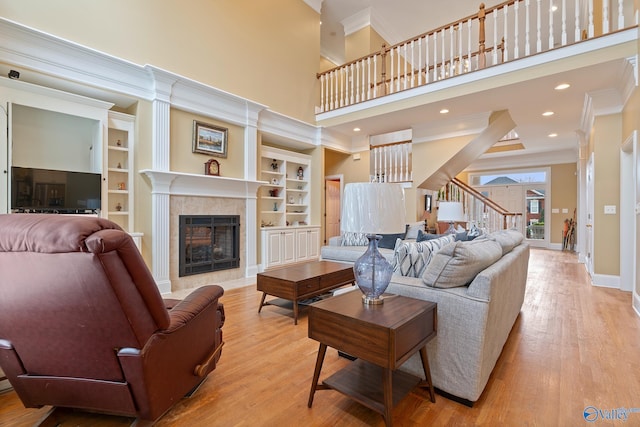 living room featuring built in shelves, crown molding, a tiled fireplace, wood finished floors, and baseboards