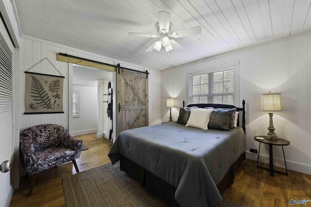 bedroom with a barn door, baseboards, ceiling fan, and wood finished floors