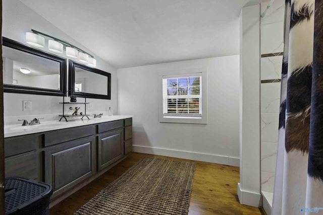 full bath featuring lofted ceiling, a sink, wood finished floors, baseboards, and double vanity