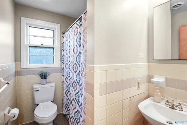 bathroom with visible vents, toilet, a sink, wainscoting, and tile walls